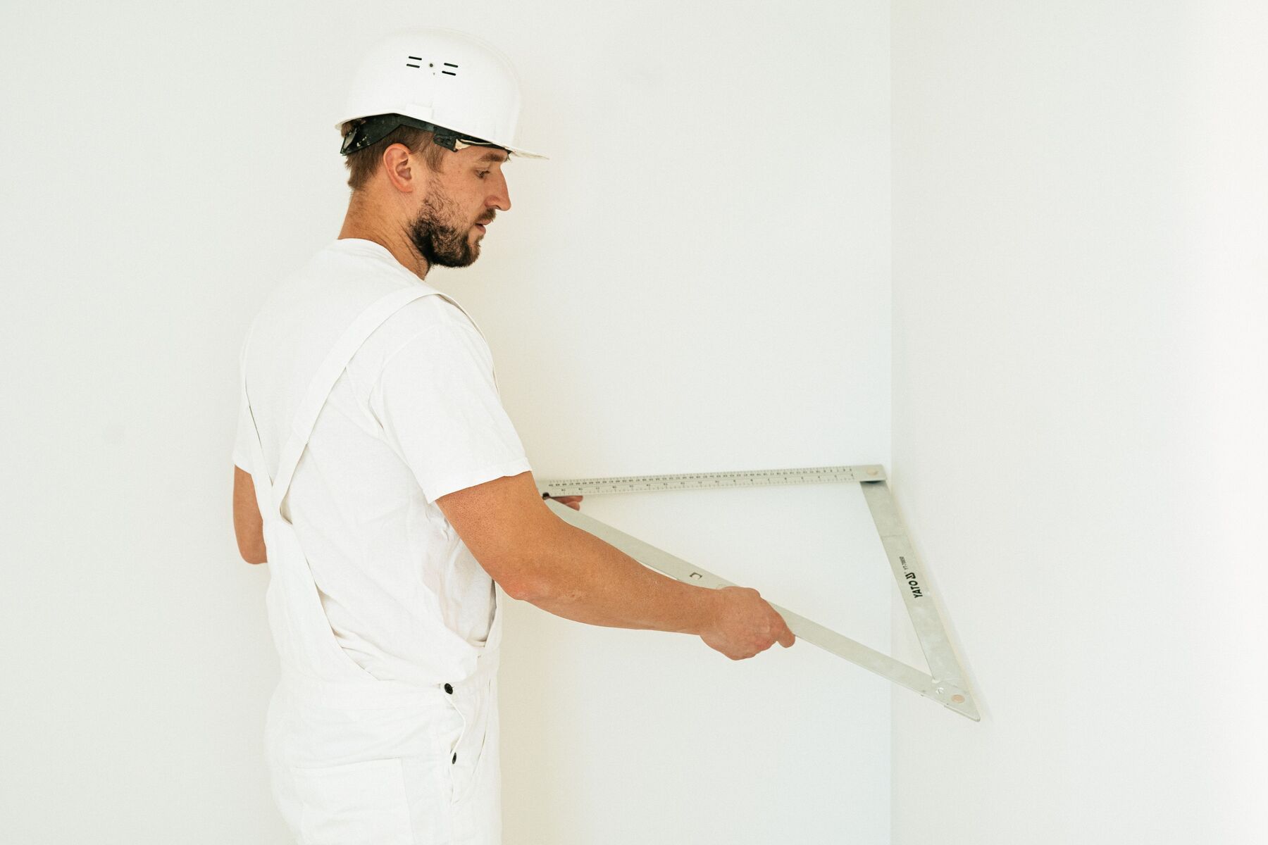A plasterer checking a freshly finished white wall corner with a folding square